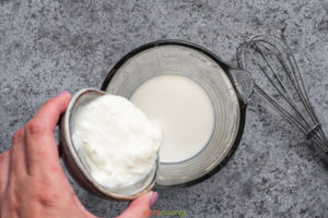 Adding yogurt starter to milk in glass cup