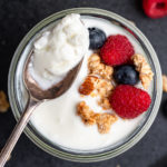 Spoon full of yogurt from a cup topped with berries and granola