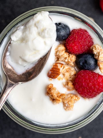 Spoon full of yogurt from a cup topped with berries and granola