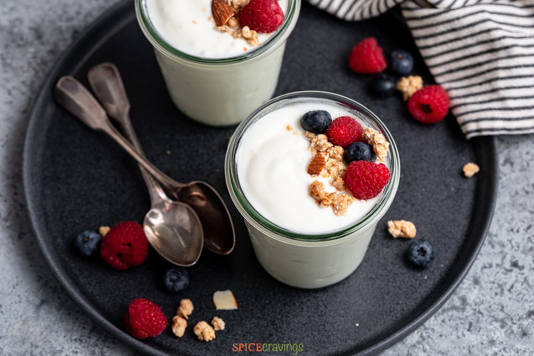 Two glass jars with yogurt topped with berries and granola