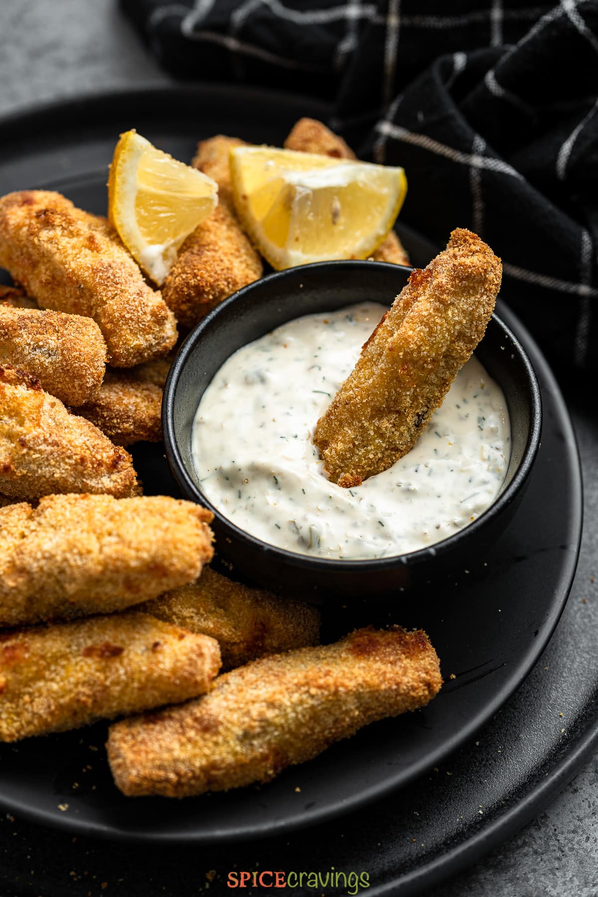 plate of air fryer fish sticks with one dipped in lemon caper sauce