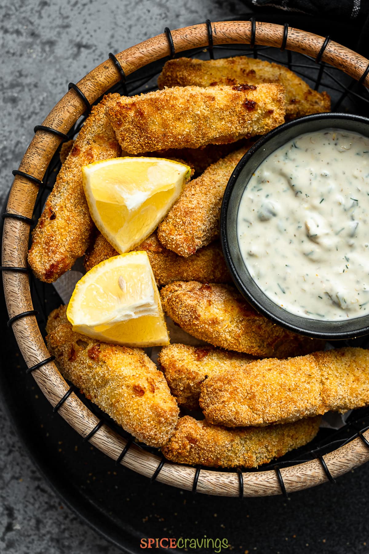 air fried fish sticks in a basket with a bowl of lemon caper sauce garnished with lemon slices