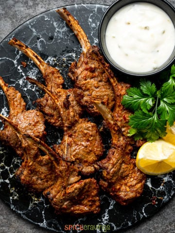 lamb chops on plate with tzatziki, parsley and lemon wedges