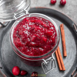 overhead shot of jar of cranberry chutney next to cinnamon sticks and cranberries
