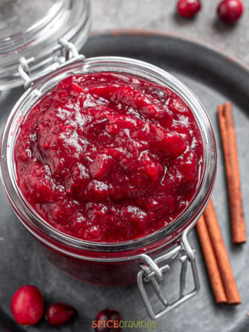 overhead shot of jar of cranberry chutney next to cinnamon sticks and cranberries