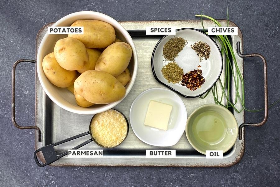 Potatoes, spices, cheese, oil, butter and chives on metal tray
