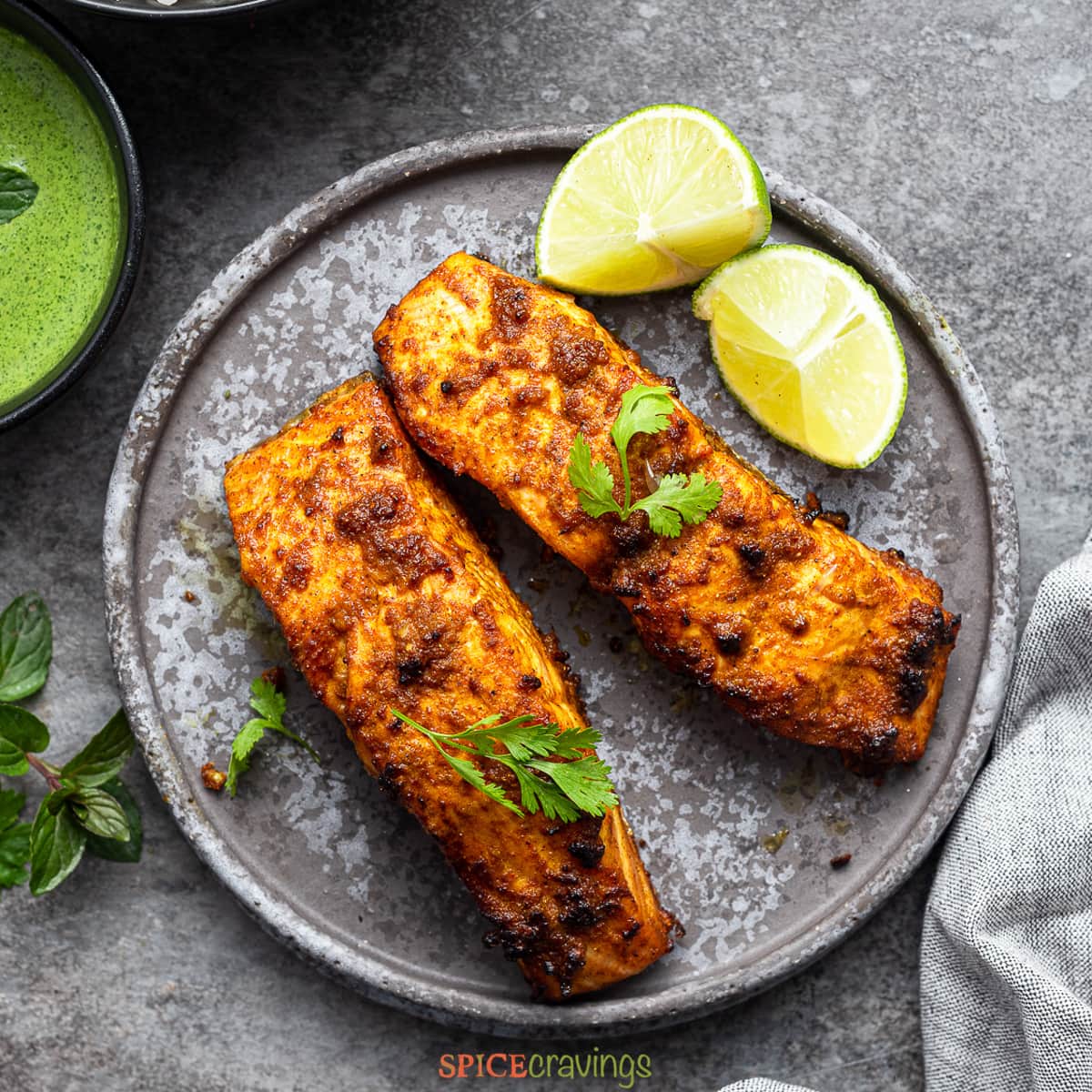 two tandoori salmon steaks on gray plate with lime wedges