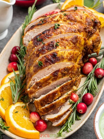 sliced turkey breast on platter with orange slices, cranberries and rosemary