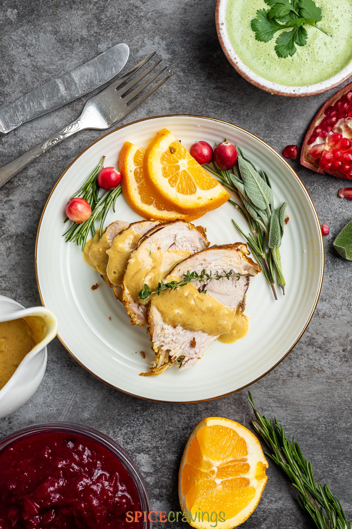 four slices turkey breast on white plate with orange slices, cranberrries, fresh herbs