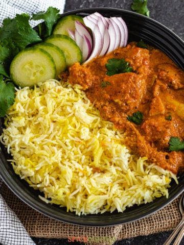 bowl filled with saffron rice, butter chicken, with sliced veggies, and greens for garnish