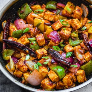 Paneer, green pepper, red chilies in skillet with sliced spring onions