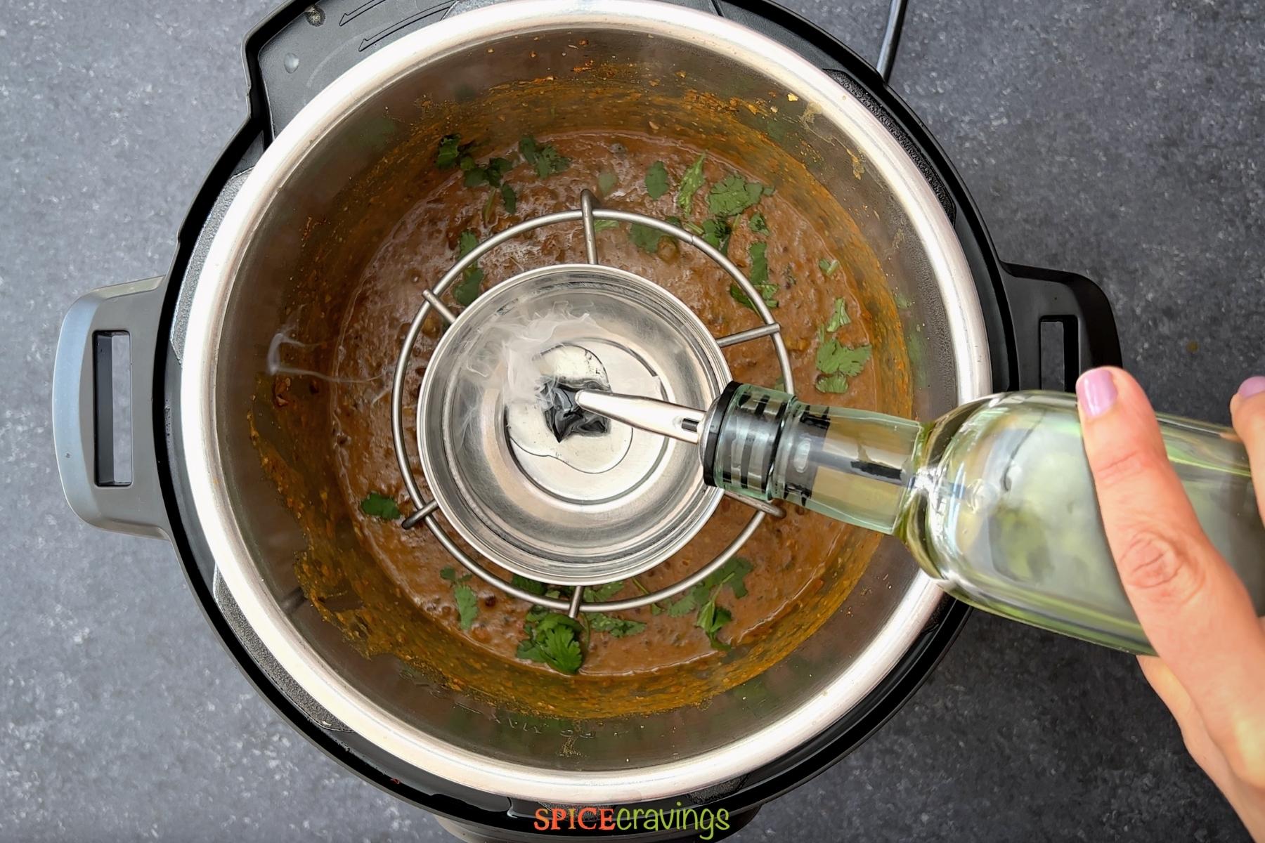 pouring oil from bottle over charcoal set in stainless steel bowl in instant pot
