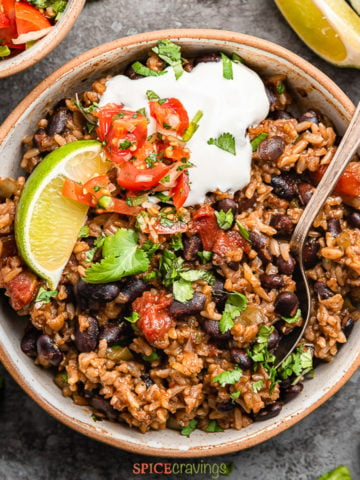 Bowl of Mexican rice and beans garnished with salsa, sour cream and cilantro