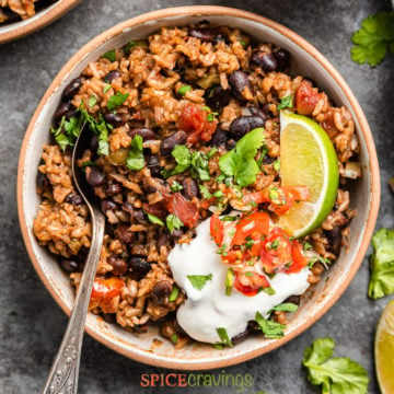 overhead of a bowl of Mexican rice and beans garnished with lime, cilantro, tomato, and sour cream