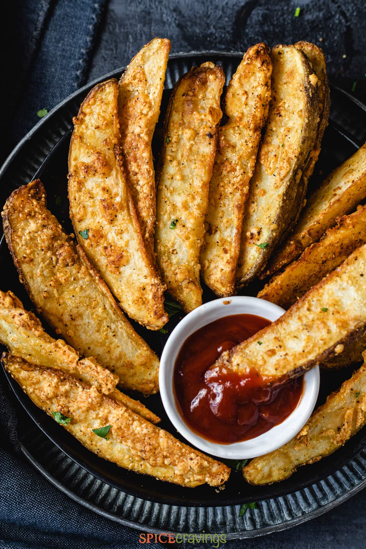 overhead of a plate filled with potato wedges with one being dipped into a bowl of ketchup
