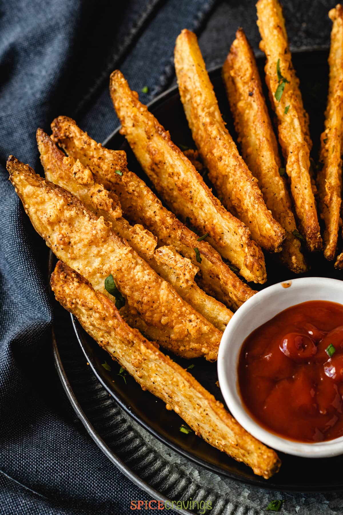 air fried potato wedges lined up on a plate with a bowl of ketchup overhead