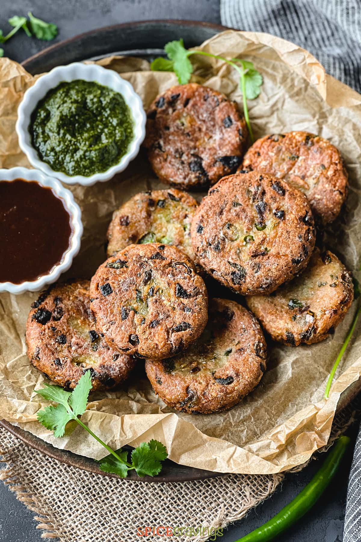 indian spiced potato patties layered onto a serving platter with two bowls of chutney