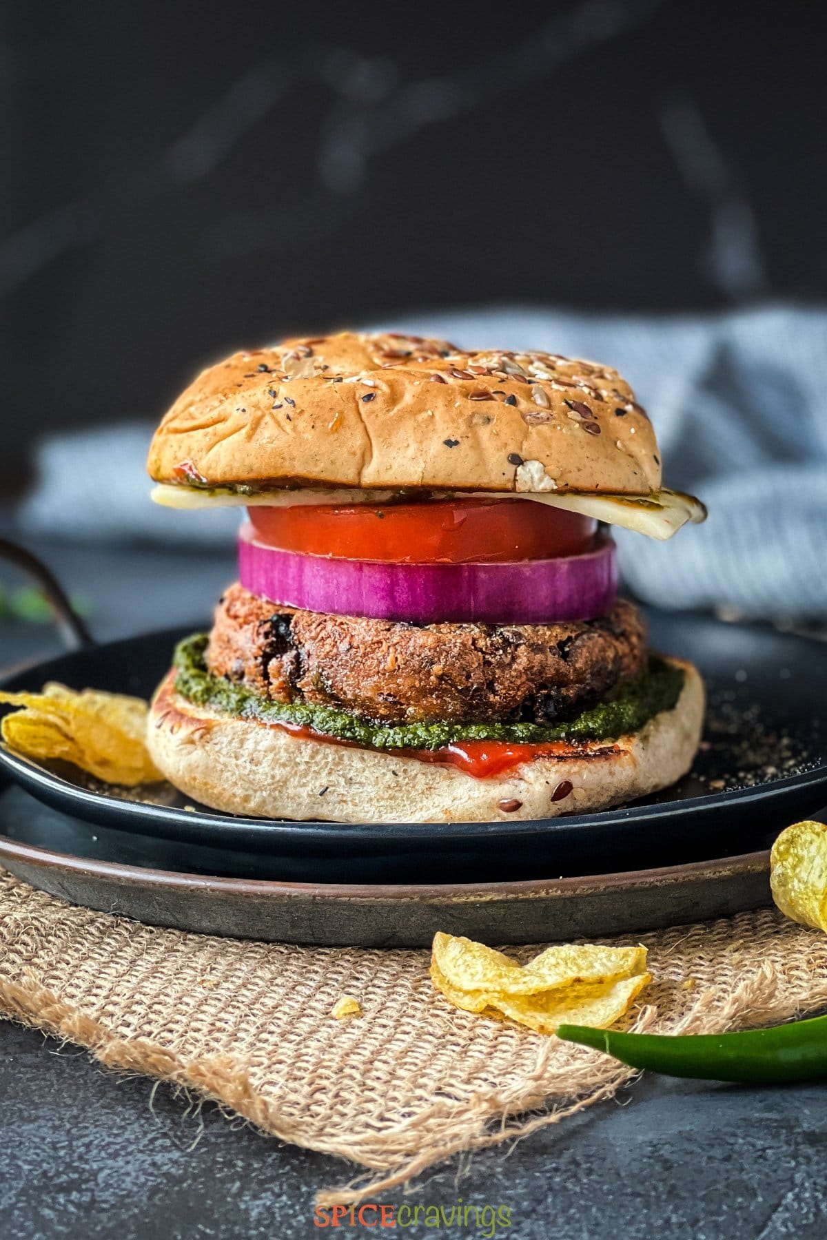 Burger on a plate with aloo tikki patty, onion, tomato, cheese and chutney