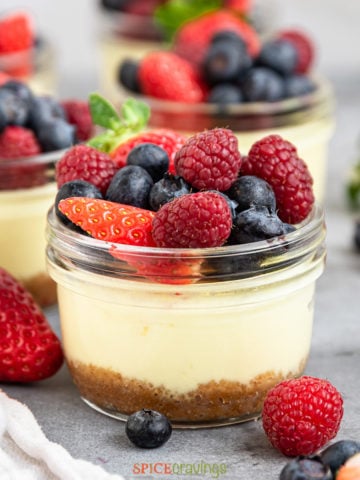 closeup of a jar of cheesecake topped with berries with other mini cheesecakes in the background