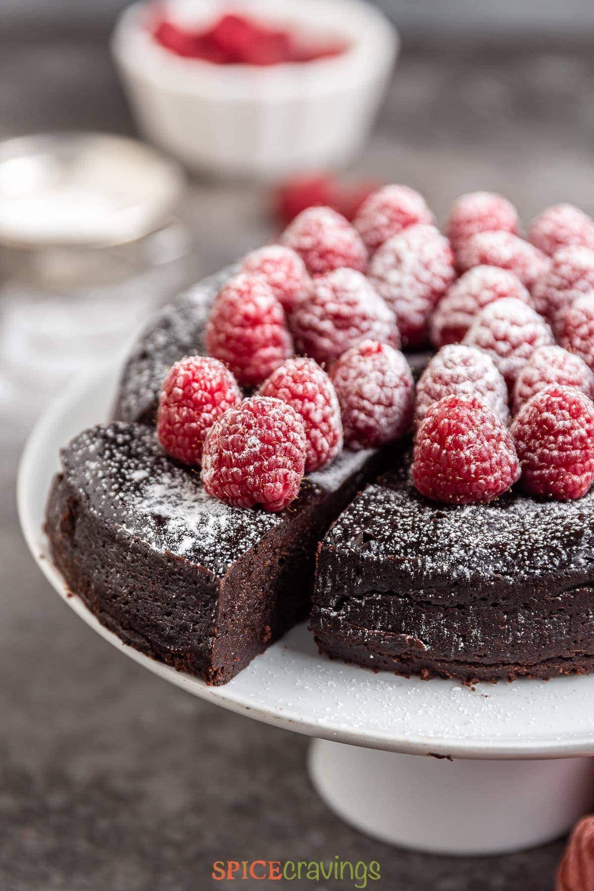sliced chocolate flourless cake topped with raspberries and powdered sugar