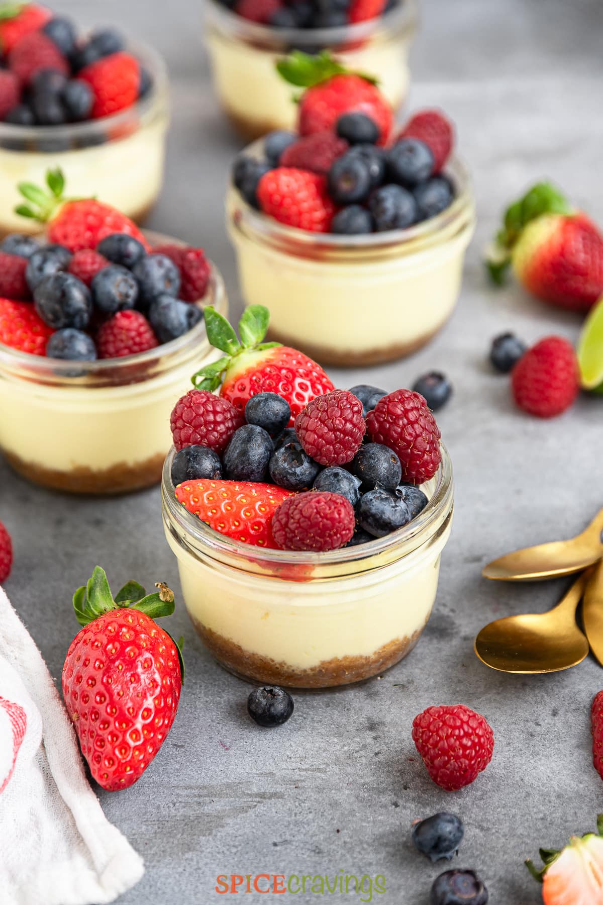 five mini cheesecake jars lined on a gray countertop overhead topped with mixed berries