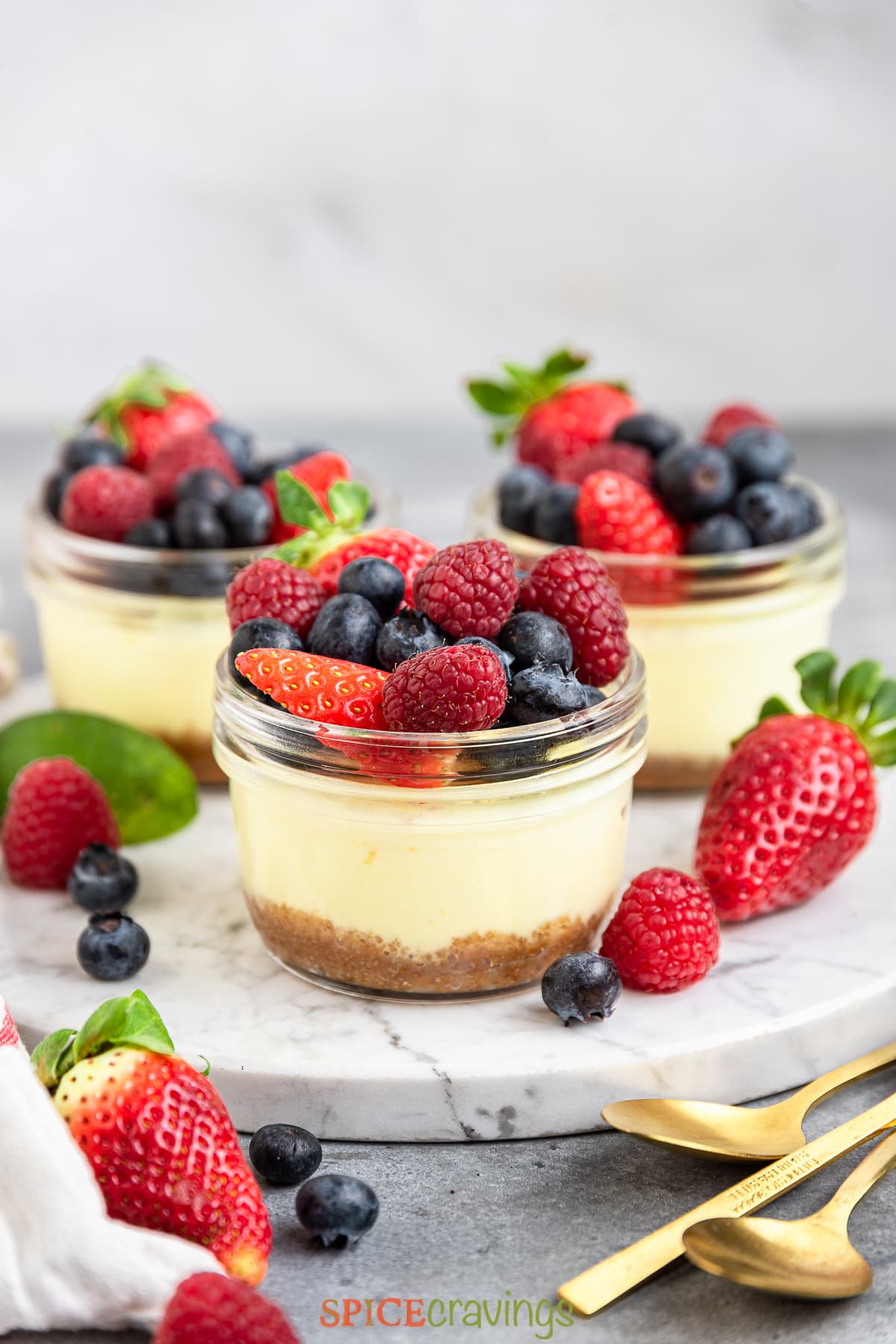 side view of three mini cheesecake jars topped with mixed berries on a marble serving platter