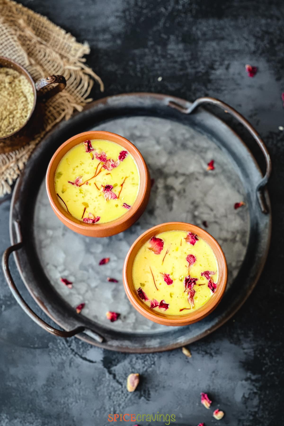Two clay cups with yellow colored milk with rose petals
