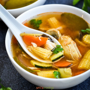 Soup spoon loaded with baby corn, carrot, chicken and zucchini
