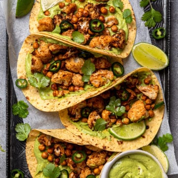 four roasted cauliflower tacos on baking sheet with green goddess on side