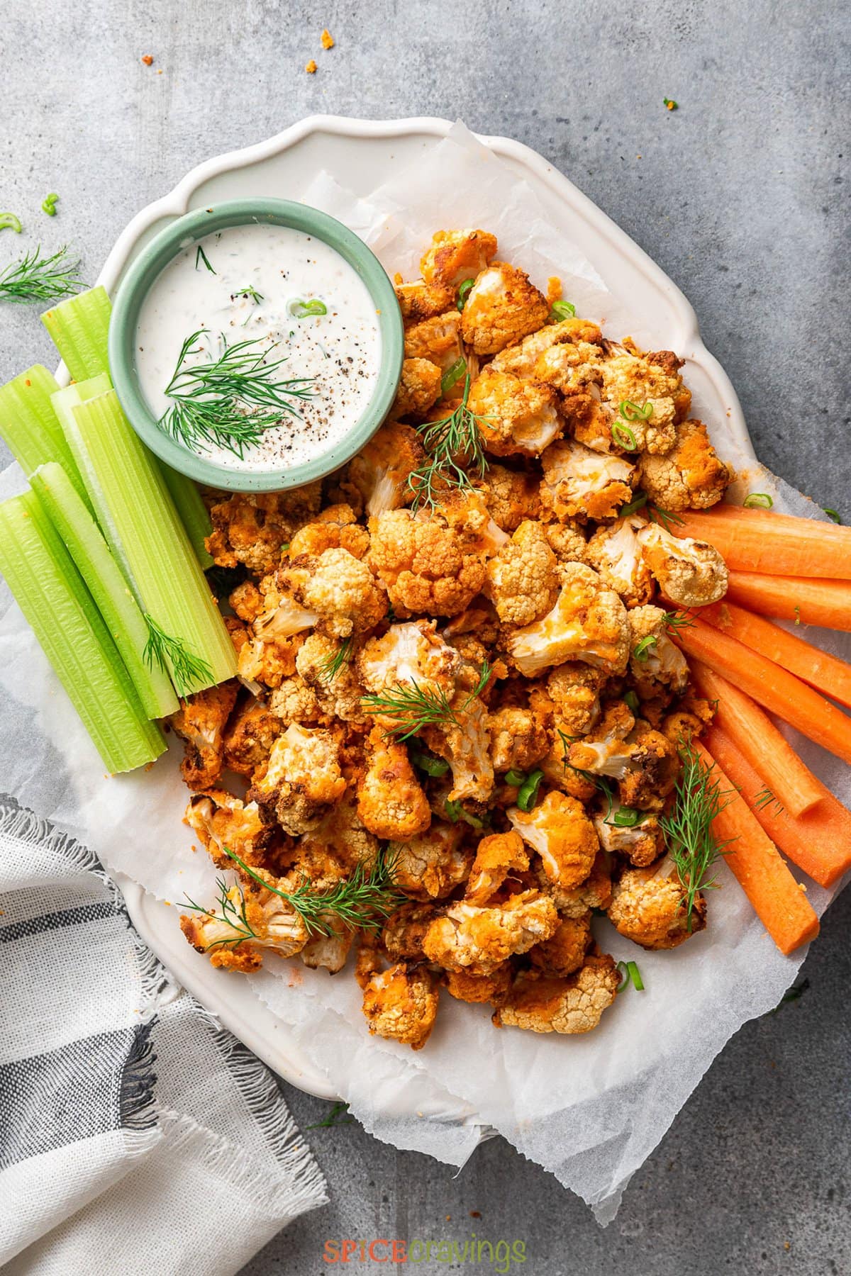 buffalo cauliflower bites on white platter with celery, carrot sticks and creamy sauce with dill