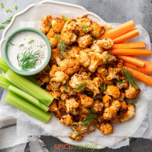 crisp cauliflower wings on white platter with celery, carrot sticks and creamy sauce