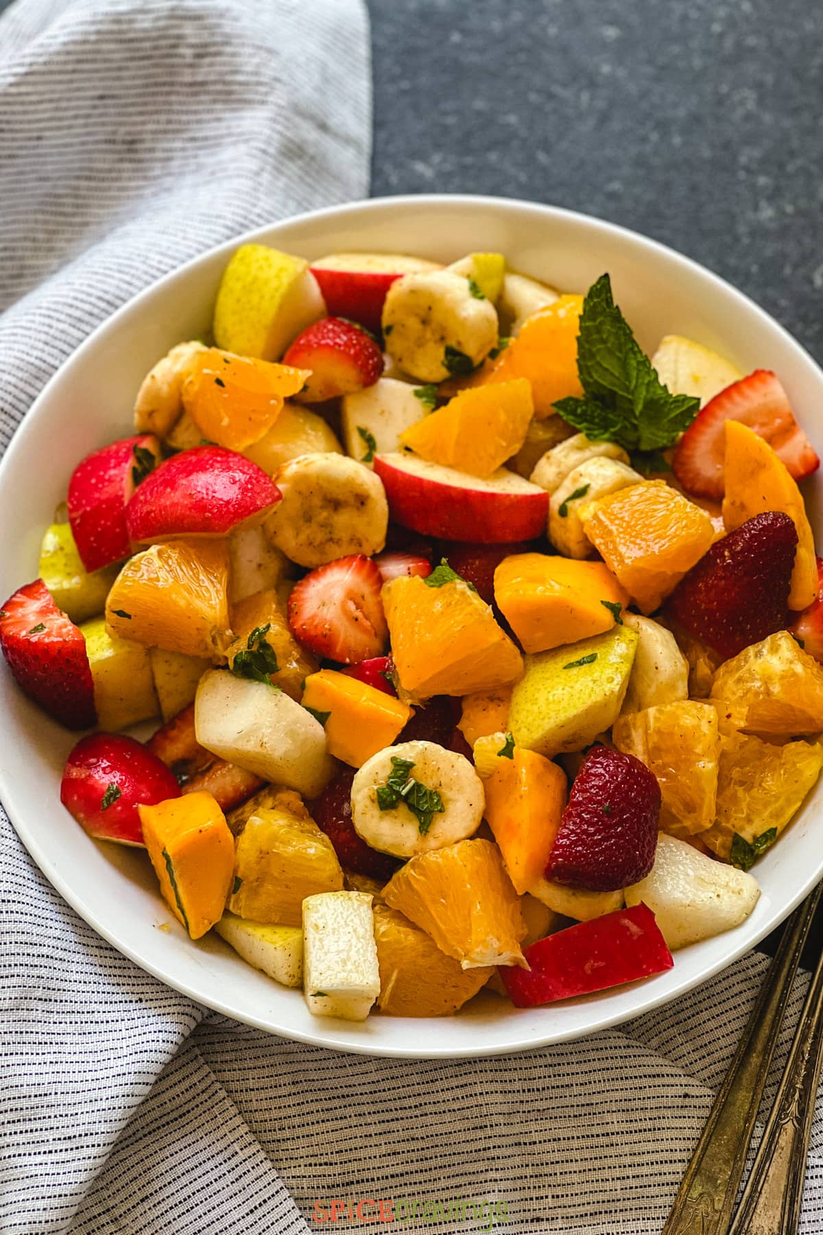 Fruit salad seasoned with spices and mint in white bowl