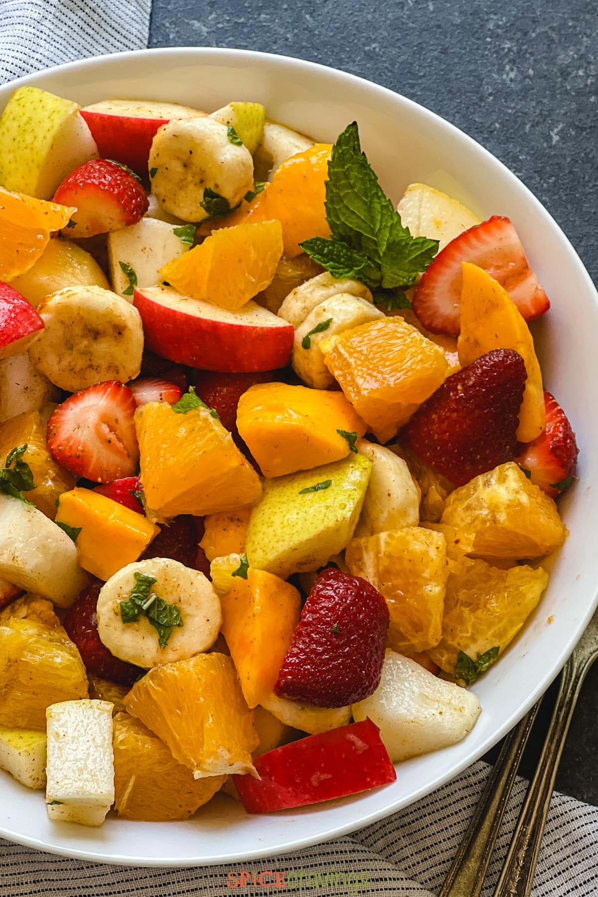 Chopped fruit salad in white bowl seasoned with spices and mint