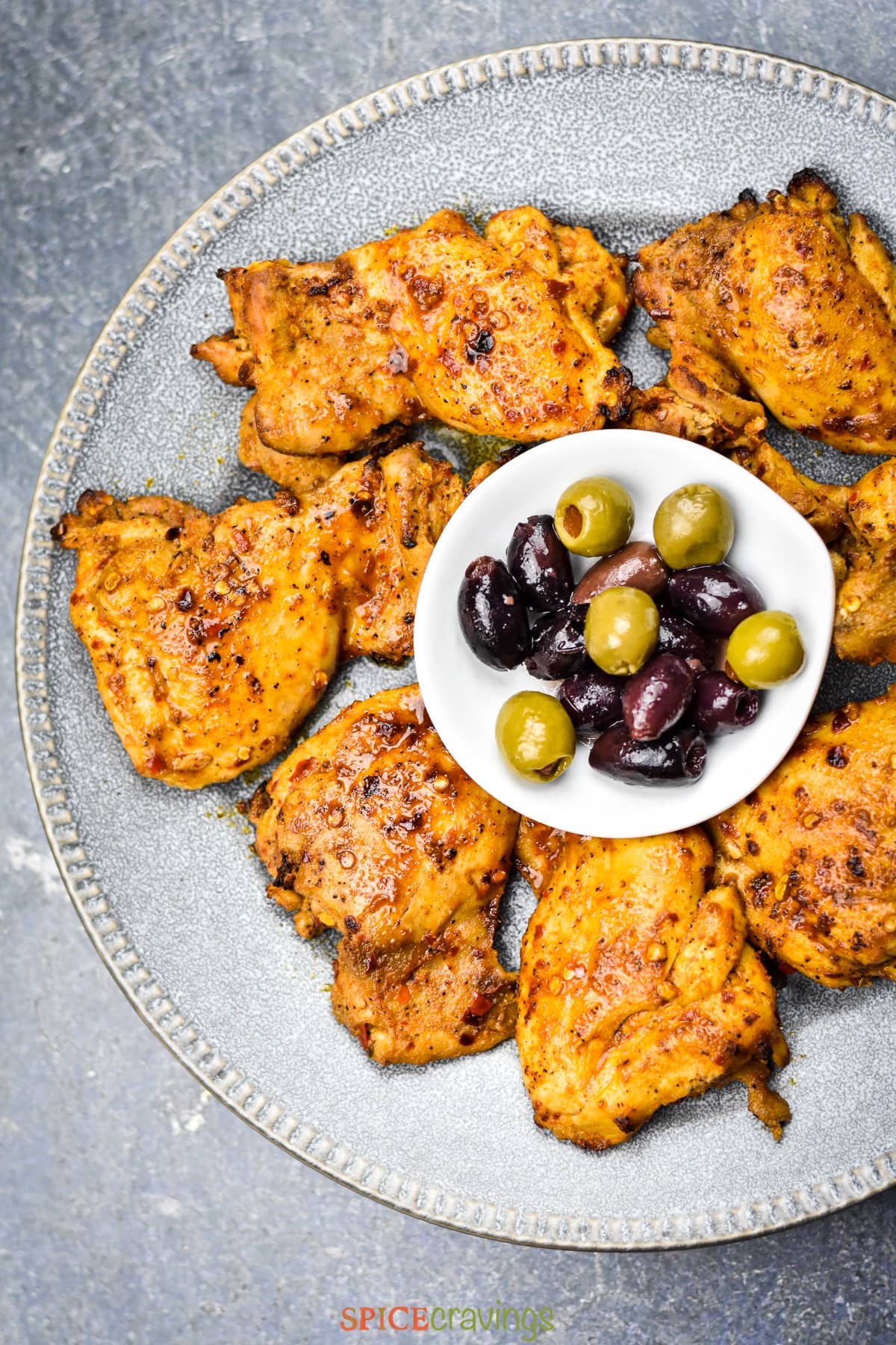 Greek chicken recipe on gray plate with bowl of kalamata olives in the middle