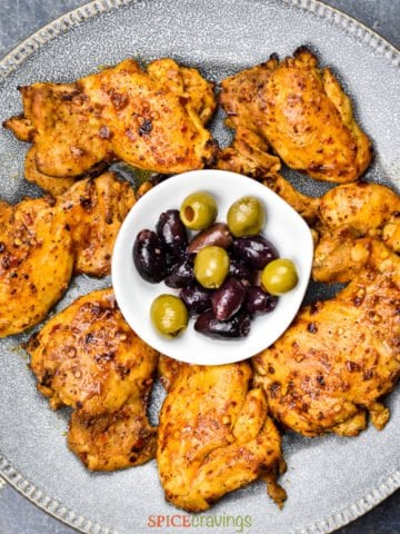 Greek chicken recipe on gray plate with bowl of kalamata olives in the middle