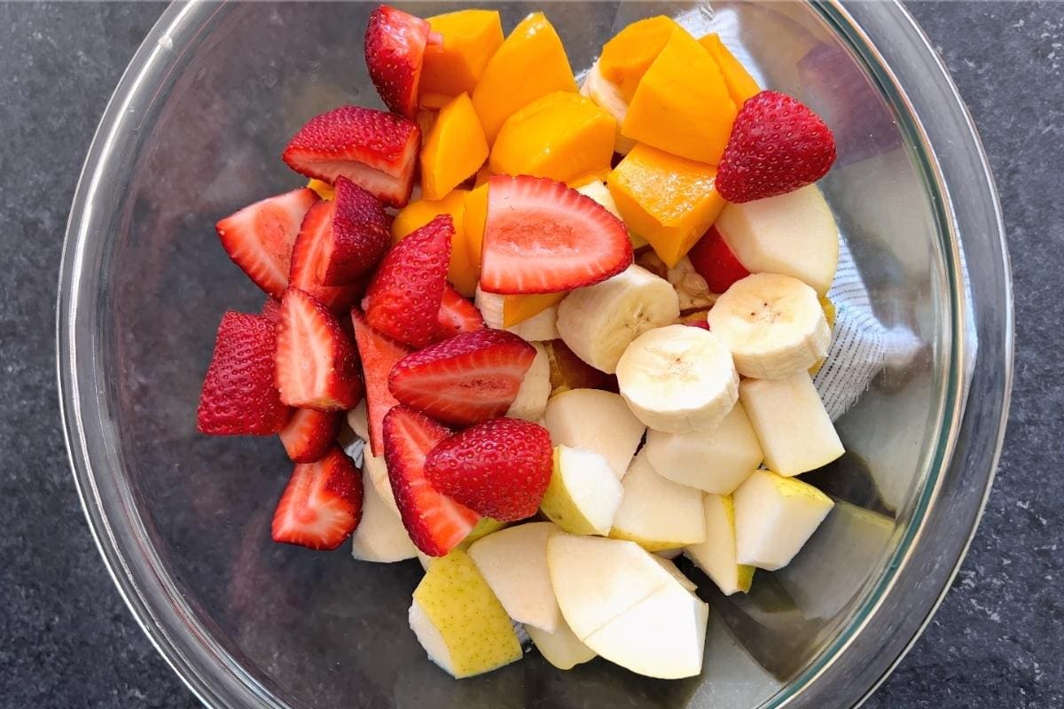 Cut strawberries, banana, pear, apple and mango in bowl