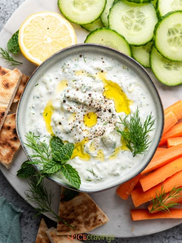 tzatziki sauce recipe in white bowl with cut vegetables on the side