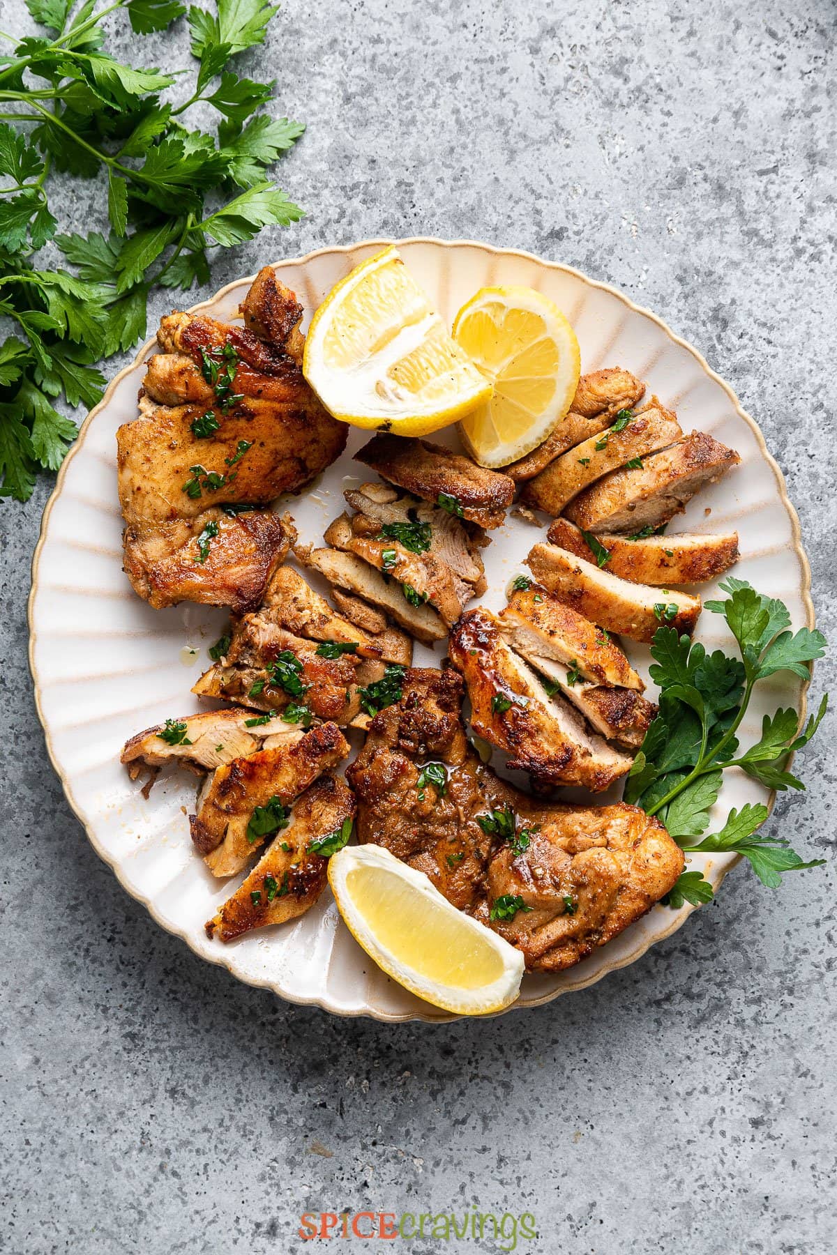 sliced Greek chicken thighs on white platter with lemon wedges