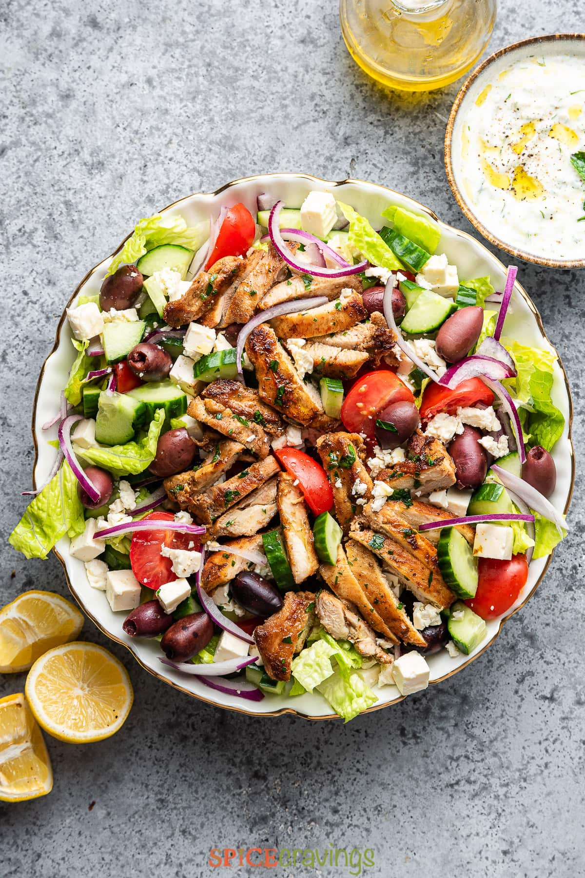 chicken greek salad in large white serving bowl with dressing and lemon on the side