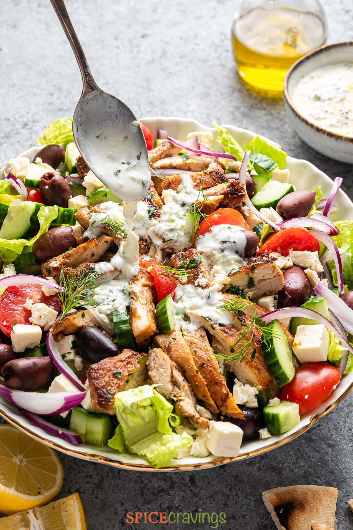 spooning tzatziki dressing over greek salad with chicken