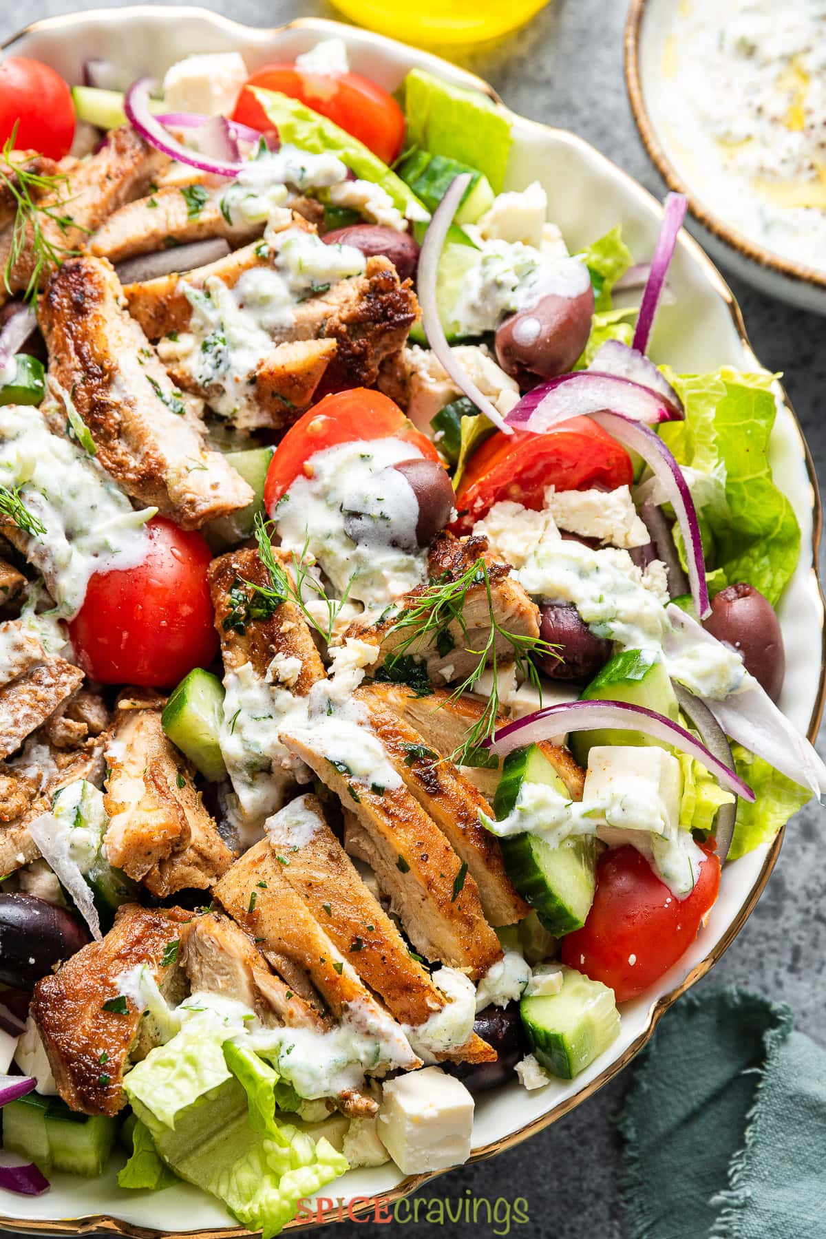 grilled chicken salad recipe in large white bowl with onion, cucumber, olives, and feta