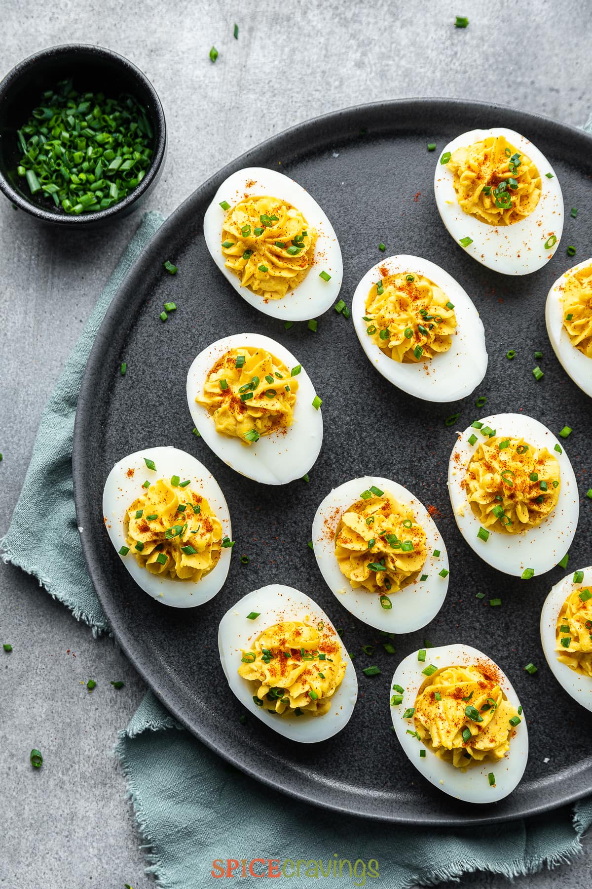 spicy deviled eggs garnished with chives on black platter