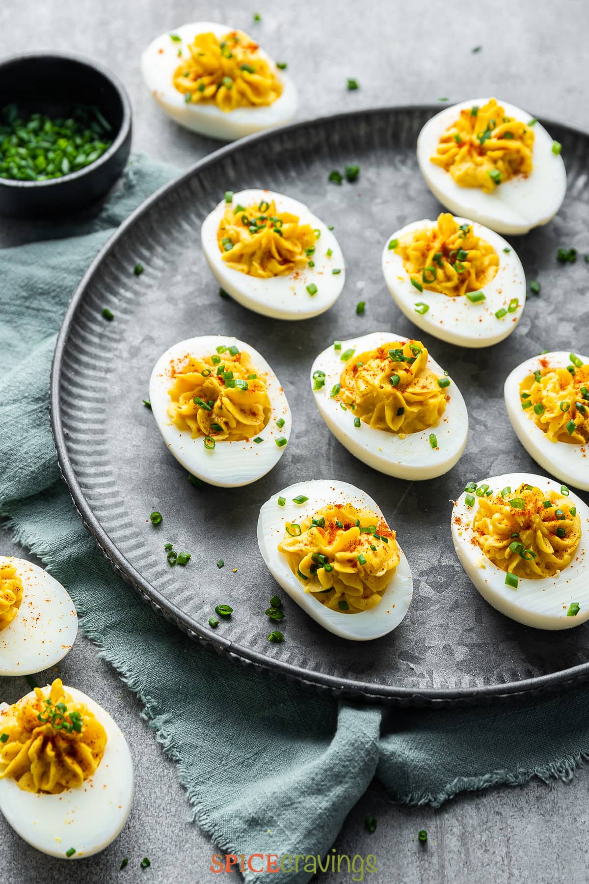 spiced deviled eggs garnished with chives on gray plate