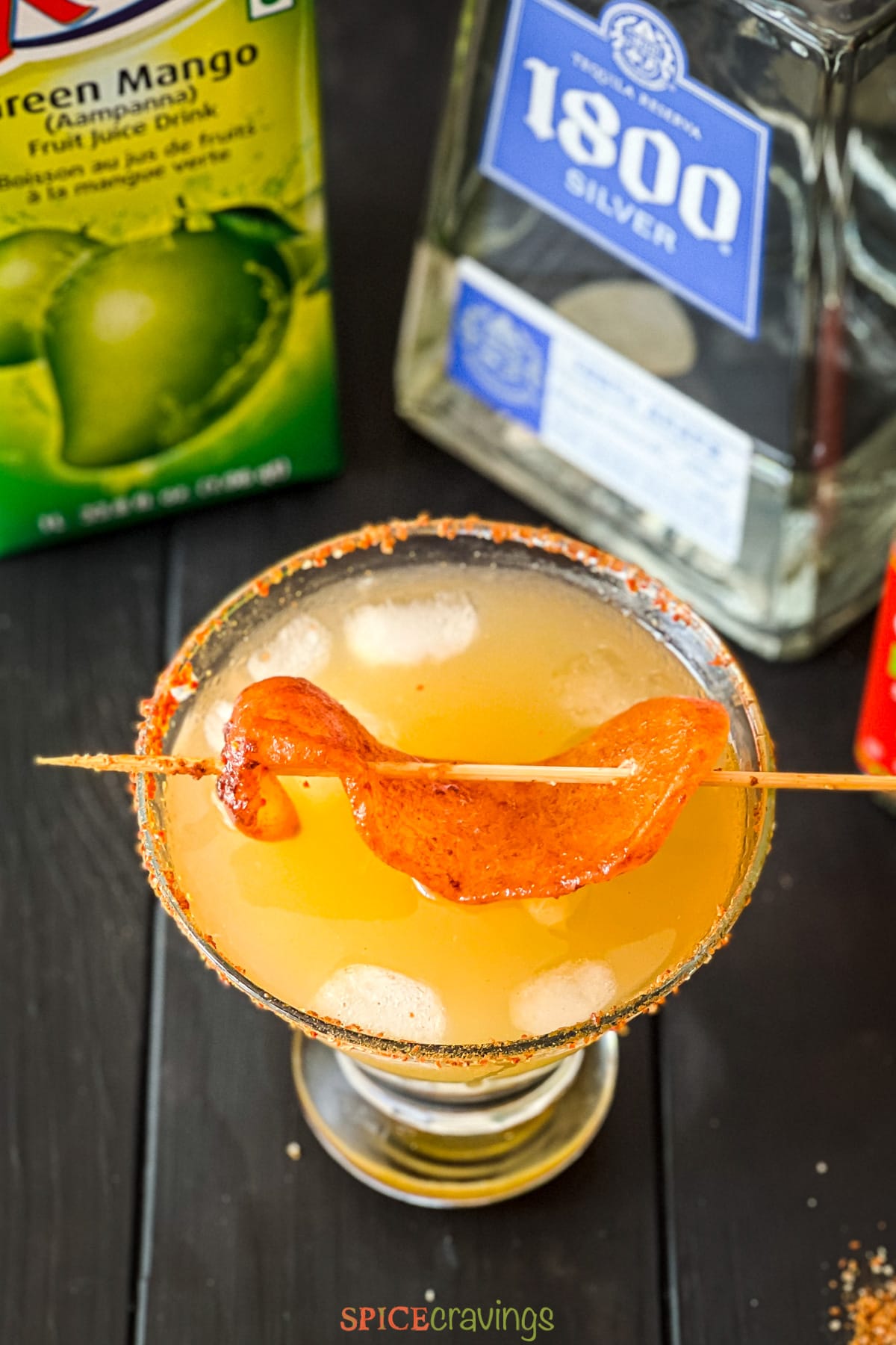 glass with spicy yellow drink topped with chili mango skewer