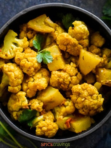 Curried cauliflower and potato in black bowl garnished with cilantro
