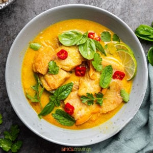 Yellow fish curry in grey bowl with basil and mint leaves garnish