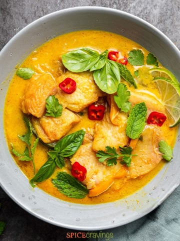 Yellow fish curry in grey bowl with basil and mint leaves garnish