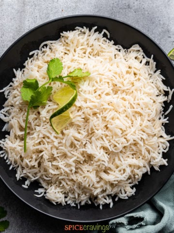coconut milk rice in black bowl garnished with cilantro and lime wedge