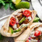 two falafel pita sandwiches on round plate with cucumbers and tomatoes