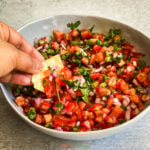 Hand dipping in bowl of pico de gallo with tortilla chip
